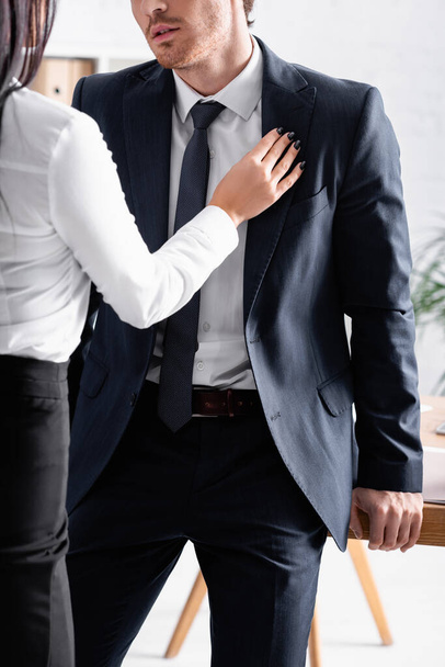 Teilansicht der Sekretärin berührt Anzug des Geschäftsmannes beim Flirten mit ihm im Büro - Foto, Bild