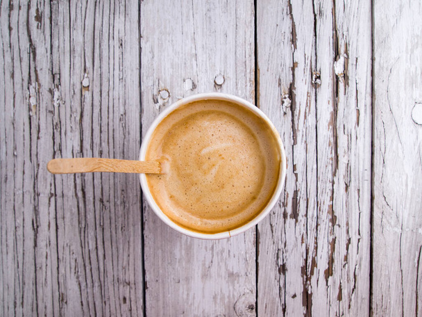 Top view on a disposable cardboard glass with coffee and a wooden stick for stirring sugar. One americano with milk. - Photo, Image