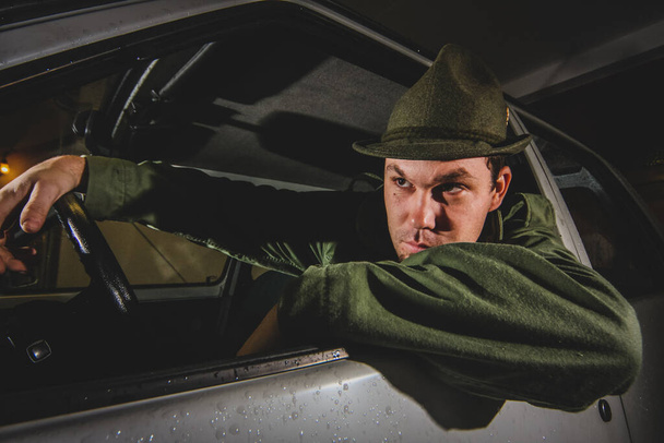 Uma pessoa vestida de verde como um caçador, com um chapéu está sentado em um carro e posando. - Foto, Imagem
