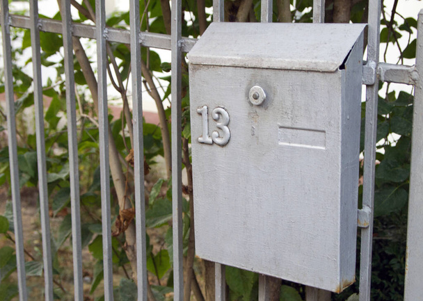 Один серый металлический почтовый ящик висит на заборе. Номер "13" ставится на почтовый ящик.. - Фото, изображение