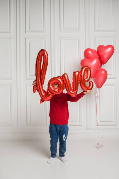mały chłopiec pokrył się czerwonym balonem miłość na białym tle z czerwonymi balonami serca - Zdjęcie, obraz