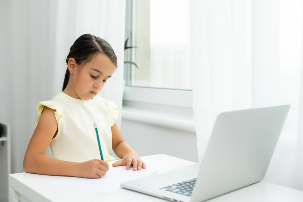 Litttle girl looking at laptop screen with expression of surprised and excitement. Smart, smilling little girl taking notes . Communication in business concept. - Φωτογραφία, εικόνα