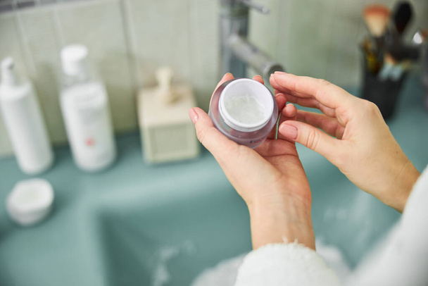 Woman using cosmetics face cream in bathroom - Foto, imagen