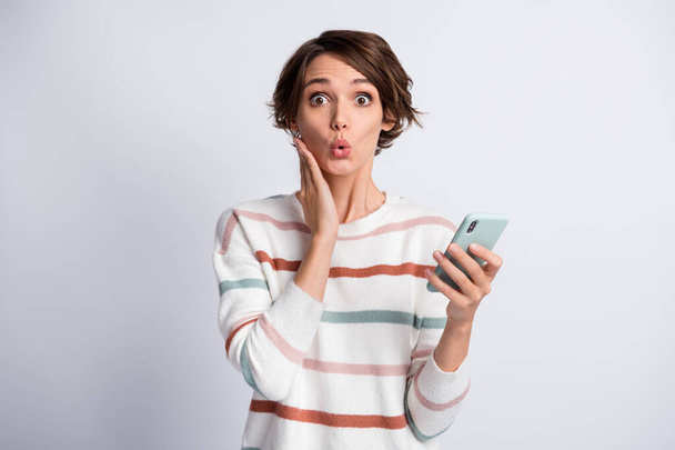 Photo of excited funny young lady wear striped sweater holding modern gadget arm cheek isolated grey color background - 写真・画像