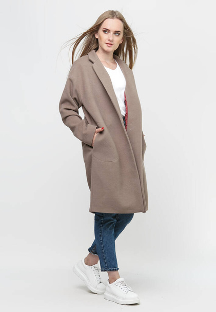 hermosa modelo posando en un abrigo largo marrón sobre un fondo blanco. Grabado en estudio. Concepto de publicidad de ropa. - Foto, Imagen