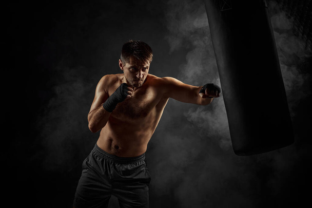 Male boxer punching in boxing bag on black background - Photo, Image