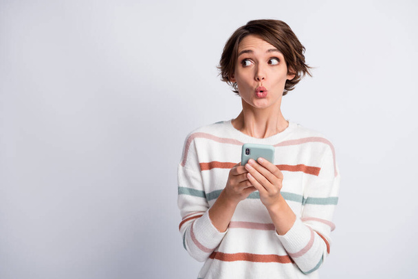 Photo of excited cute young lady wear striped sweater holding modern gadget looking empty space isolated grey color background - 写真・画像