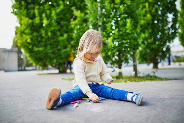 Adorable toddler girl drawing with colorful chalks on asphalt. Outdoor activity and creative games for small kids - Фото, зображення