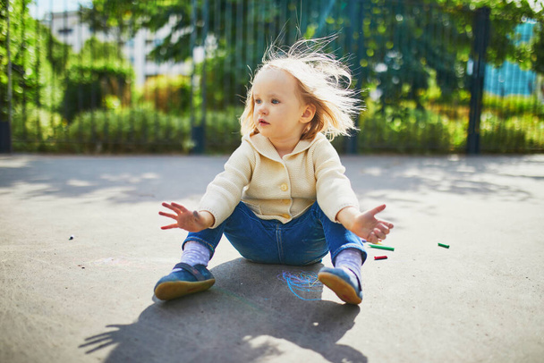 Adorable toddler girl with dirty hands after drawing with colorful chalks on asphalt. Outdoor activity and creative games for small kids - Fotó, kép