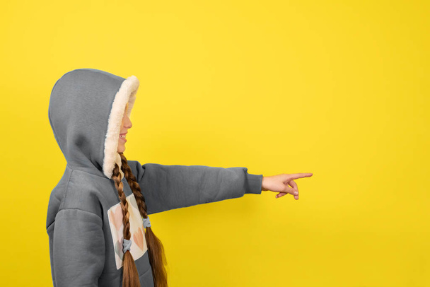 Teen beautiful girl in santa hat smiling and pointing her finger. Banner toned in trendy Ultimate Grey and Illuminating yellow colors of 2021. - Φωτογραφία, εικόνα