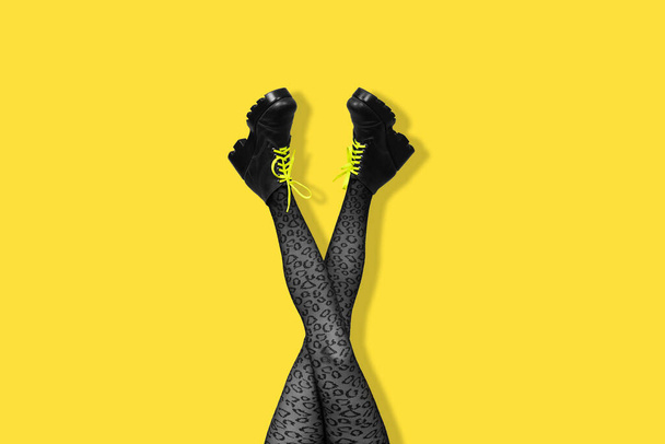 Nuevas botas femeninas grises con cordones de color amarillo brillante en piernas largas y delgadas cruzadas de mujer en medias grises aisladas sobre fondo amarillo. Concepto de arte pop con botas de trabajo pesado. Banner con espacio de copia. - Foto, imagen