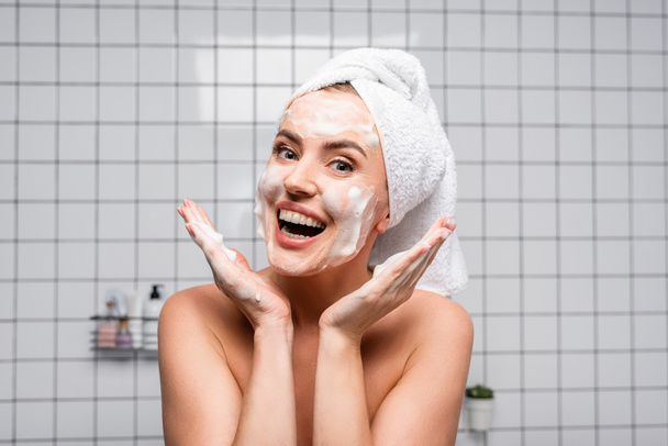 excited woman with naked shoulders applying foam cleanser in bathroom - 写真・画像