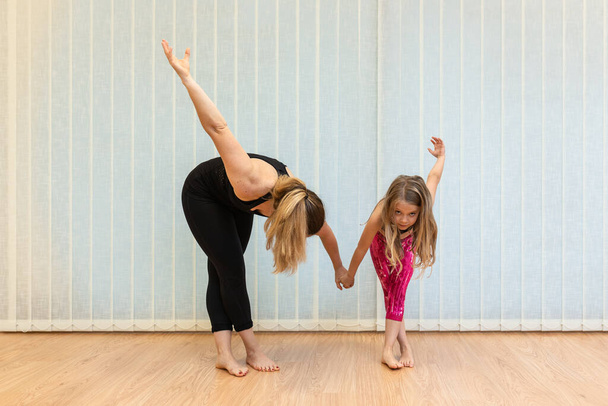 Anne yoga eğitmeni ve kızı denge egzersizleri ve esneme hareketleri yapıyorlar. - Fotoğraf, Görsel