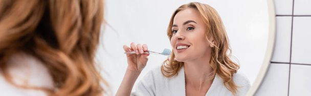 donna allegra che tiene lo spazzolino da denti con dentifricio vicino allo specchio, banner - Foto, immagini