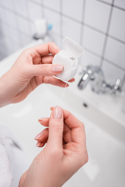 cropped view of woman holding plastic container with dental floss in bathroom  - Fotografie, Obrázek