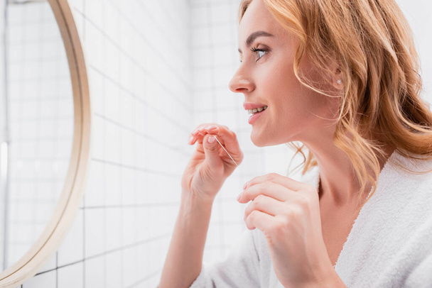 mujer alegre mirando al espejo y sosteniendo hilo dental - Foto, Imagen
