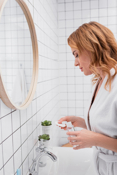 vrouw houden fles met toner en katoen pad in de badkamer  - Foto, afbeelding