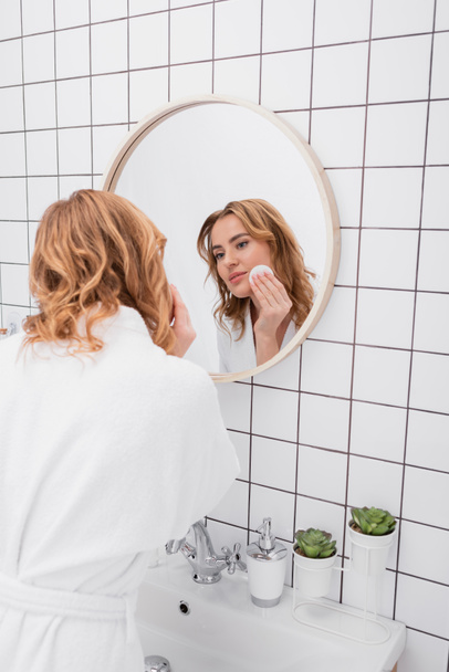happy woman applying toner on face with cotton pad and looking at mirror  - Foto, afbeelding