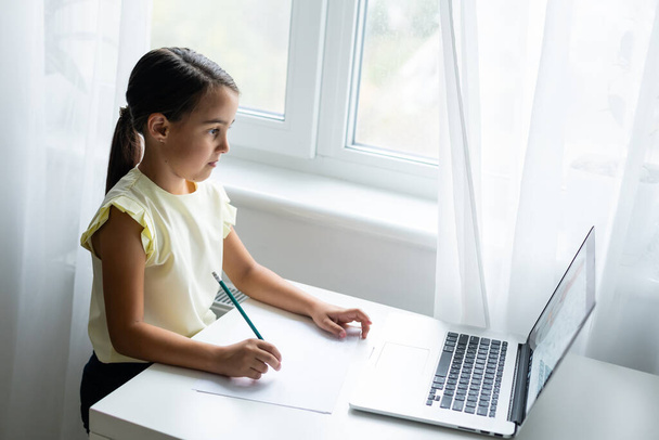 Zuhause, Freizeit, Technik und Internetkonzept - kleines Studentenmädchen mit Laptop zu Hause, kleines Mädchen nutzt Videochat - Foto, Bild