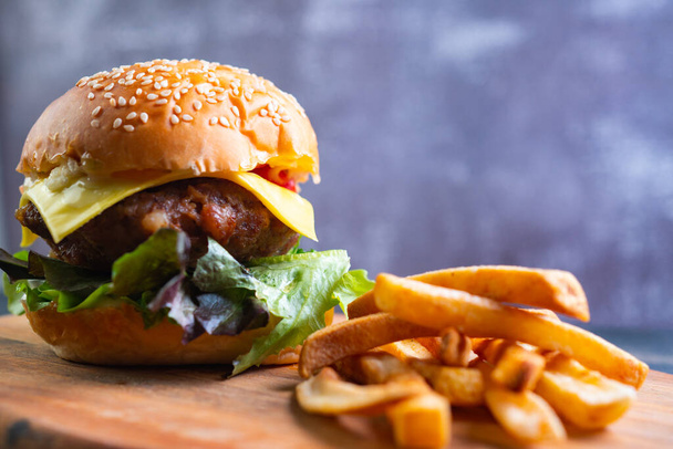 verse lekkere zelfgemaakte hamburger met verse groenten, sla, tomaat, kaas op een snijplank met friet. Vrije ruimte voor tekst - Foto, afbeelding