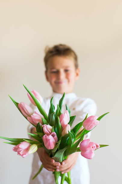 Young boy, kid, child holding in hands bouquet of pink tulips, spring flowers. Gift for mother, Valentines day concept - Valokuva, kuva