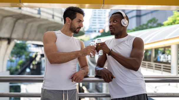 Jeune américain et noir africain LBGT couple gay toast eau à skywalk après le jogging ou la course. Sport et mode de vie sain. Charmant couple de même sexe dans la course à la diversité. - Photo, image