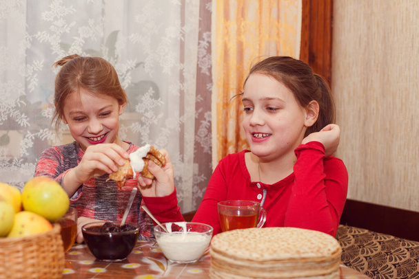 Portré két aranyos kishúgról az asztalnál palacsintával és teával, ahogy Shrovetide-ot ünneplik. - Fotó, kép
