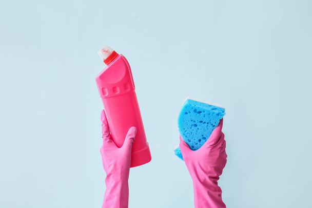 Hände in Gummihandschuhen mit Reinigungsschwamm und Reinigungsmittel auf farbigem Hintergrund - Foto, Bild
