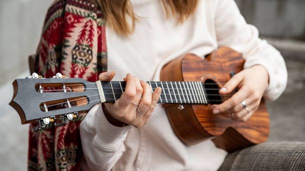Woman playing Hawaiian guitar, sings a song on vintage ukulele at home. Selective focus. Close up.	 - Foto, Bild