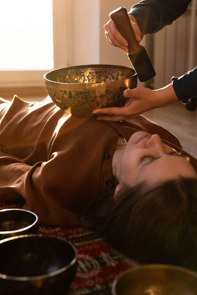 Vrouw die ontspannende massage maakt, meditatie, geluidstherapie met Tibetaanse zangkommen. Stressverlichting. Selectieve focus. Onderaanzicht.  - Foto, afbeelding