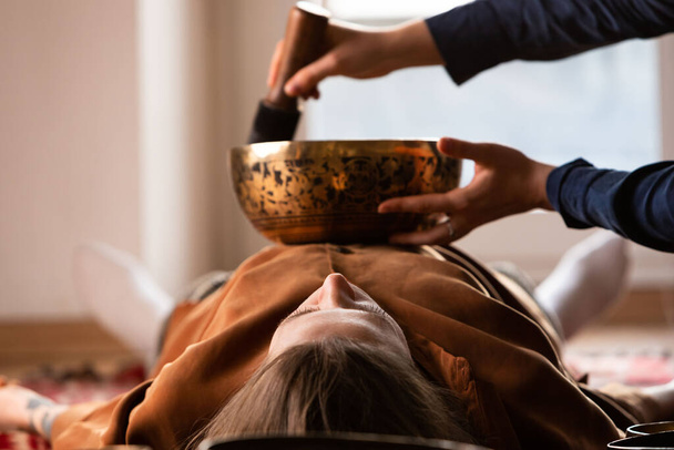Frau macht entspannende Massage, Meditation, Klangtherapie mit tibetischen Klangschalen. Stressabbau. Selektiver Fokus. Ansicht von unten. - Foto, Bild