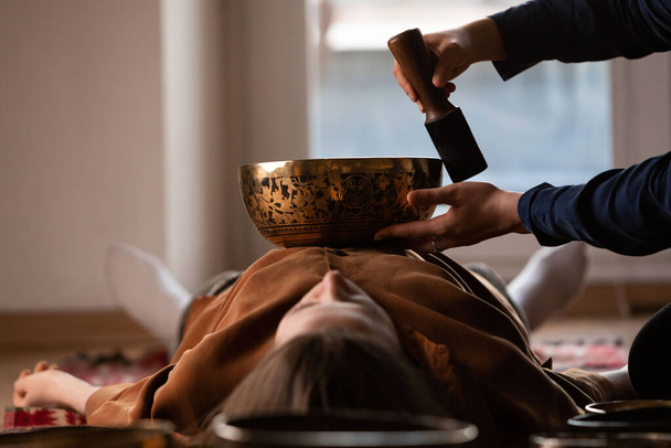 Woman making relaxing massage, meditation, sound therapy with tibetian singing bowls. Stress relief. Selective focus on female face. Bottom view. - Photo, Image
