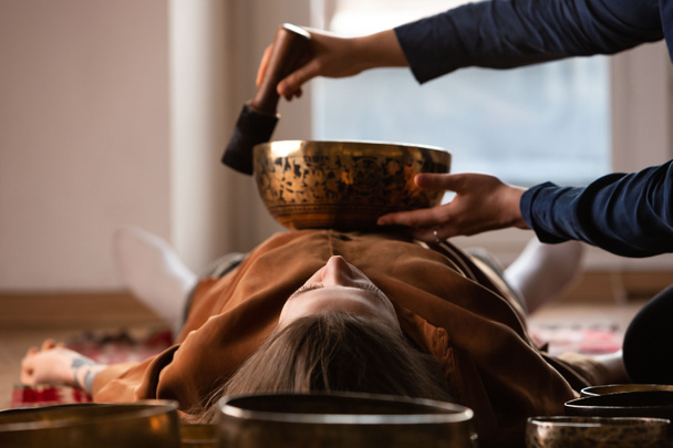 Жінка робить розслабляючий масаж, медитацію, звукову терапію з величезними співочими чашами. Стрес полегшення. Вибірковий фокус. Вид знизу
.  - Фото, зображення