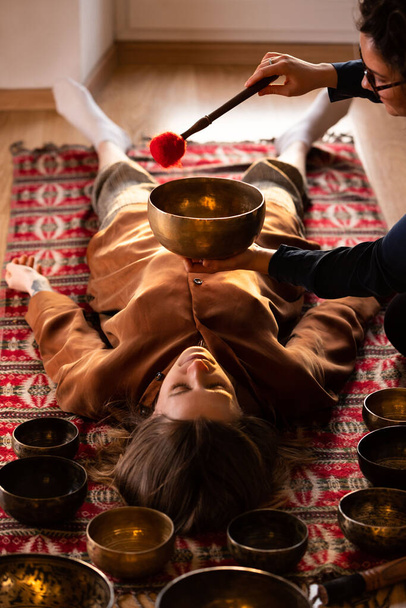Kobieta robi relaksujący masaż, medytację, terapię dźwiękową z tybetańskimi miseczkami. Zmniejszenie stresu. Wybiórcze skupienie. Widok z góry.  - Zdjęcie, obraz