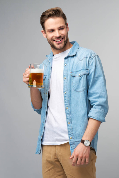 Young Man holding wearing jeans shirt holding glass of beer standing over Grey Background - Фото, зображення