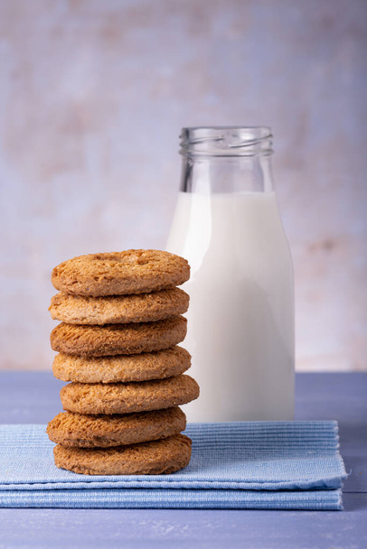 на передньому плані, на синьому столі, стопка печива з цільнозерновим борошном і пляшка коров'ячого молока
 - Фото, зображення