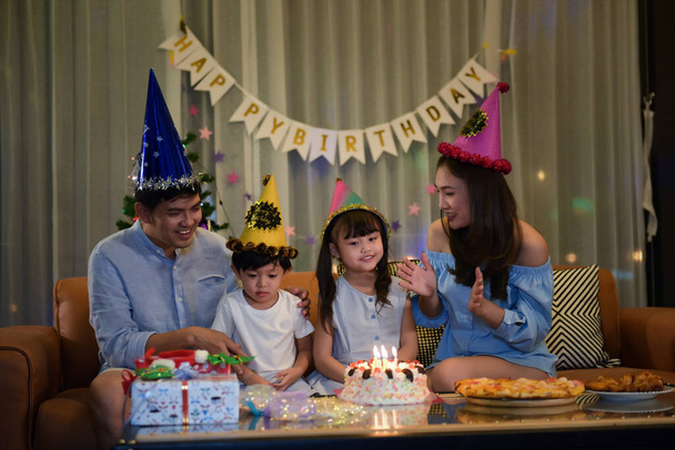 Ευτυχισμένη οικογένεια απολαμβάνει με τα μικρά δύο αδέλφια γιορτάζουν τα γενέθλια μαζί, ενώ τούρτα γενεθλίων φυσάει στο σαλόνι στο σπίτι, που είναι όμορφα διακοσμημένα και κουτί δώρου. Οι γονείς φροντίζουν τα παιδιά τους.. - Φωτογραφία, εικόνα