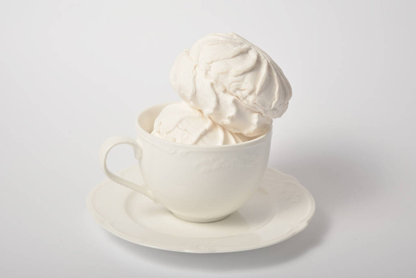 Vintage cup with two pieces of Russian traditional marshmallow dessert zefir (zephyr) souffle served on plate isolated on white background. Copy space image. Similarly with Meringue Dessert - Photo, Image