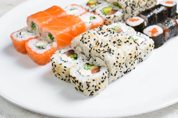 Traditional sushi rolls and maki with sesame, avocado and fish. Japanese food. Top view. On a white background. - Fotografie, Obrázek