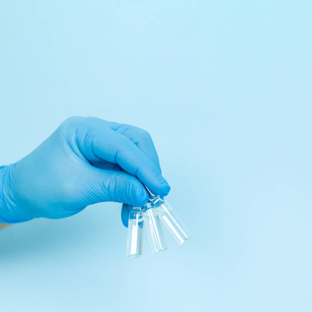 Рука доктора в перчатке с тремя ампулами медицинского стекла на синем фоне - Фото, изображение
