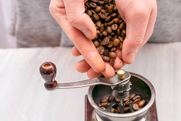 man grinds coffee beans in a manual coffee grinder hands fall asleep grain in the coffee grinder - Photo, Image