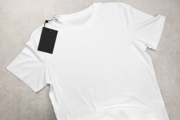 Weiße Damen Baumwolle T-Shirt-Attrappe mit Etikett. Design T-Shirt Vorlage, Print Präsentation Attrappe. Von oben betrachtet lag flach. Betonsteinhintergrund. - Foto, Bild