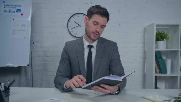 бизнесмен листает страницы блокнота и разговаривает в офисе - Кадры, видео