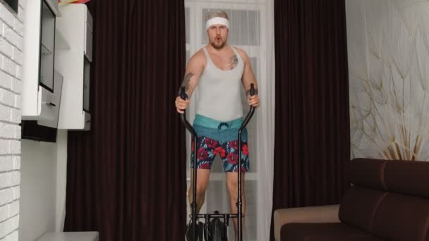 Спортсмен ретро хлопець в смішному одязі робить спортивні тренування фітнес-кардіо вправи на орбітірек будинку
 - Кадри, відео