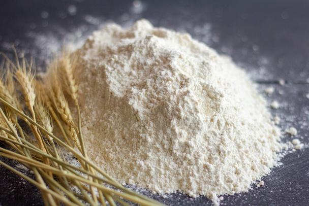 A pile of flour and ears of wheat on a dark table. - Photo, Image