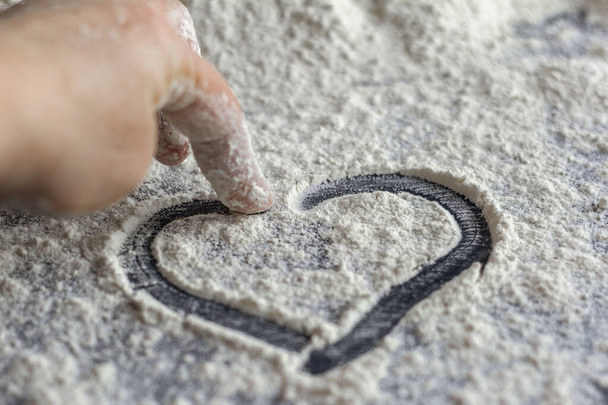 El corazón se dibuja en la harina dispersa en una mesa oscura. - Foto, imagen