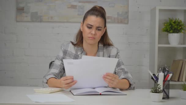 rozrušená žena drží papíry a modlí se, zatímco sedí na pracovišti  - Záběry, video