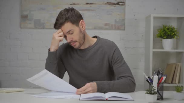 zdenerwowany człowiek patrząc na papiery podczas siedzenia w miejscu pracy  - Materiał filmowy, wideo