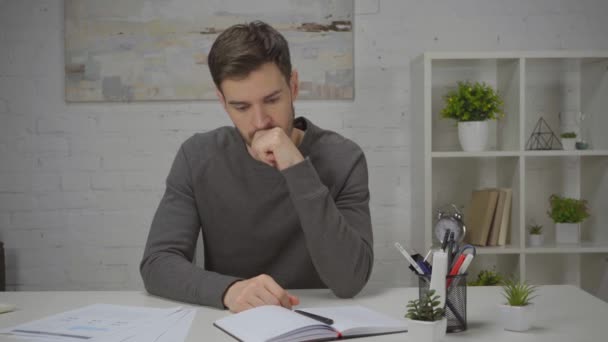 zaniepokojony człowiek patrząc na notatnik podczas pracy w domu - Materiał filmowy, wideo