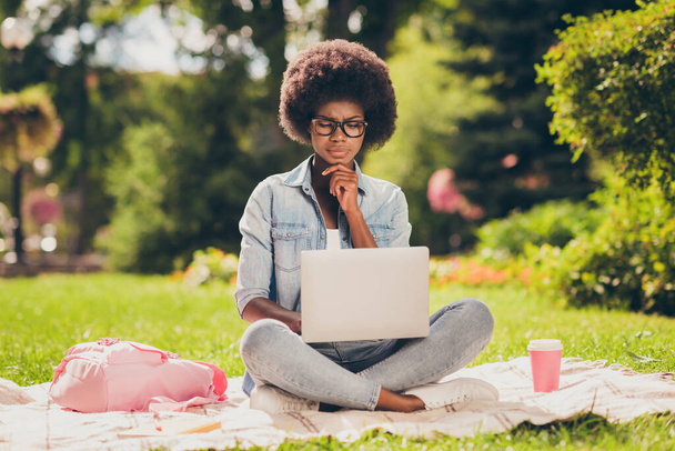 Photo portrait of black skinned girl concentrated thoughtful browsing internet with laptop sitting in park wearing glasses - Foto, Imagem